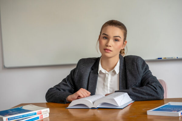 Na fotografii znajduje się dziewczyna siedząca przy biurku z rozłożonymi książkami.